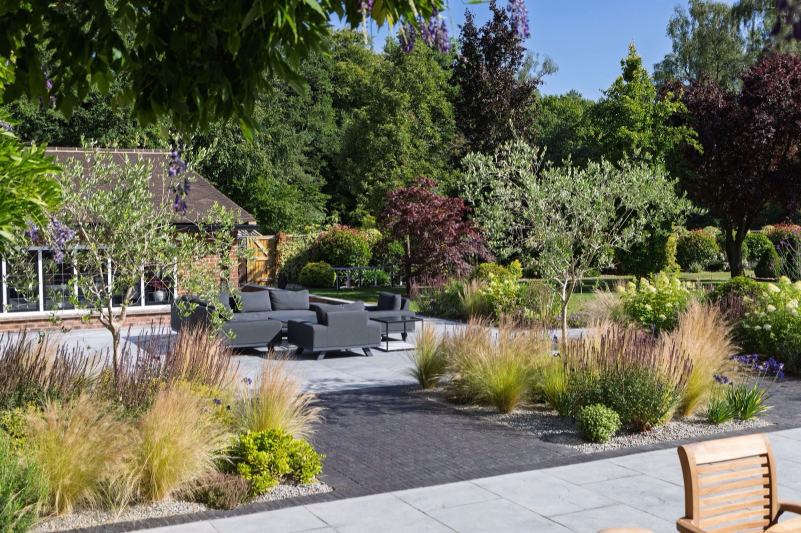 A contemporary country garden: mixed paving and setts, multi-stem trees, gravel and drifts of grasses.