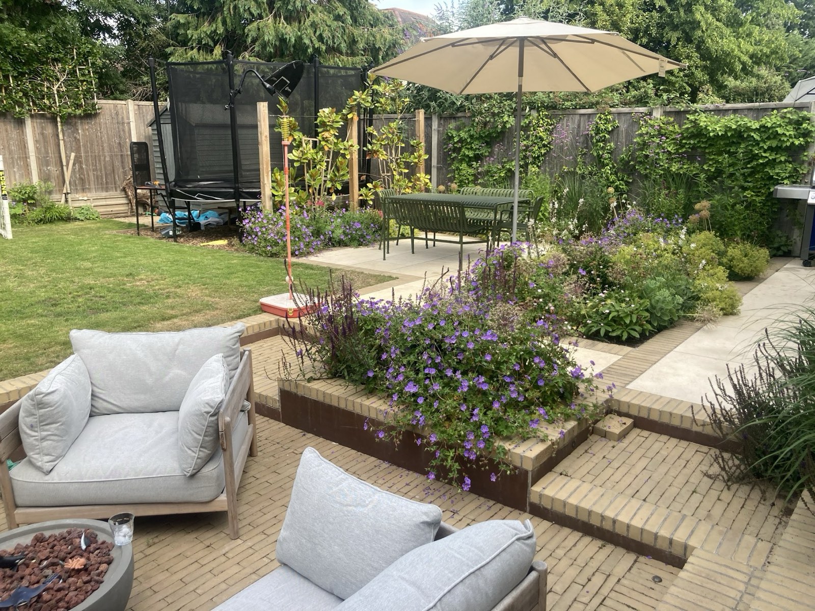 A family garden in brick and stone: raised beds thick with hardy geraniums, a dining terrace and lawn kept for playing on.