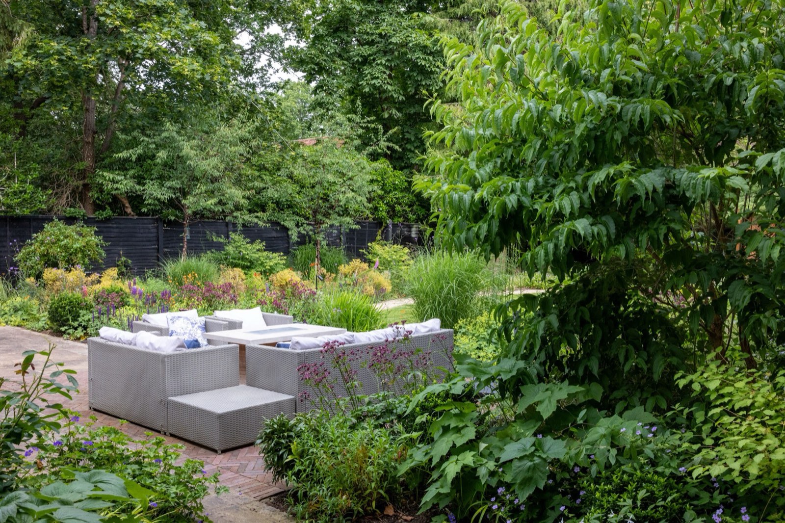 An outdoor sitting room enclosed by dark fencing, grasses and shrubs, with the boundary planted out of sight.
